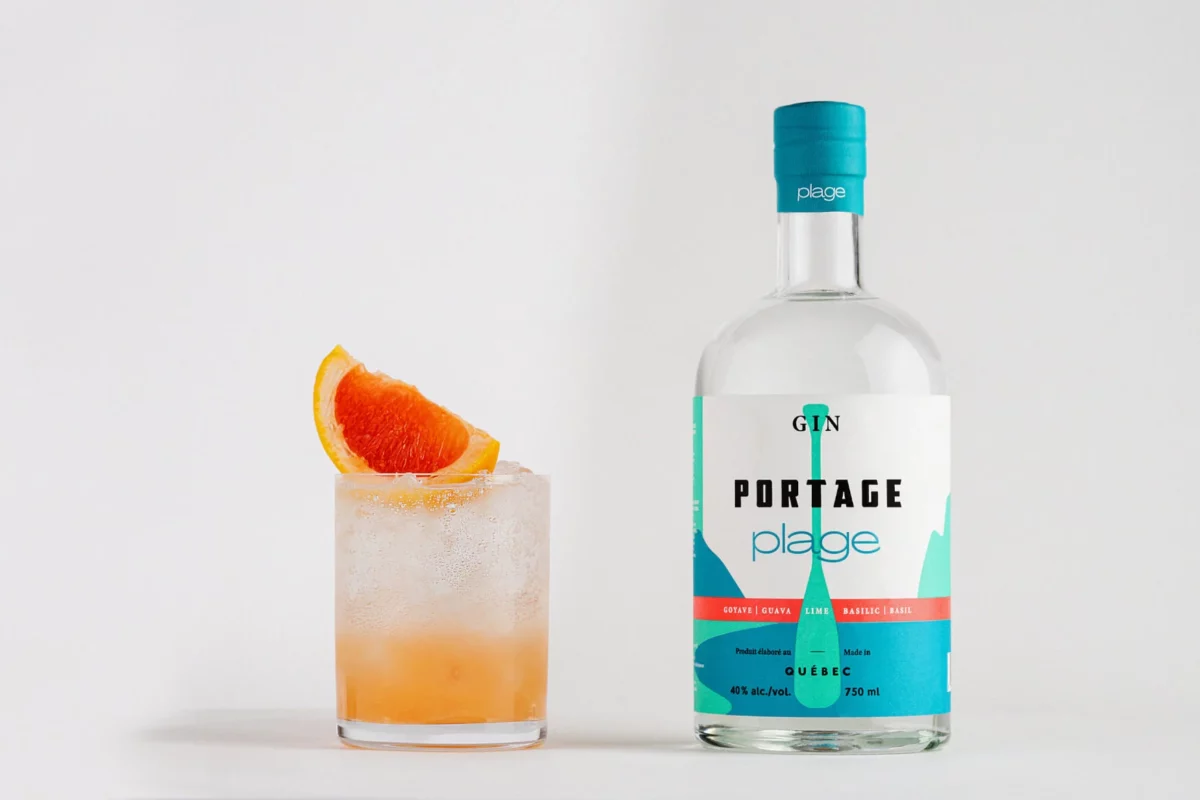 Bouteille de Gin Portage Plage avec un cocktail garni d'une tranche d'orange